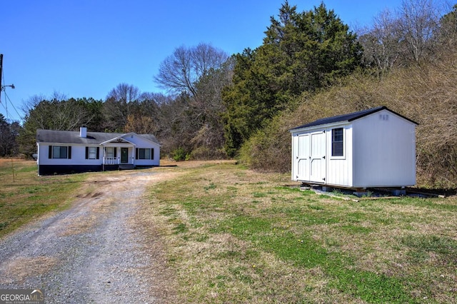 view of yard with a storage unit, an outdoor structure, driveway, and a wooded view