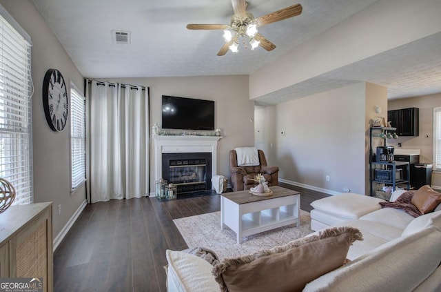 living area with vaulted ceiling, a fireplace with flush hearth, dark wood-style floors, and visible vents