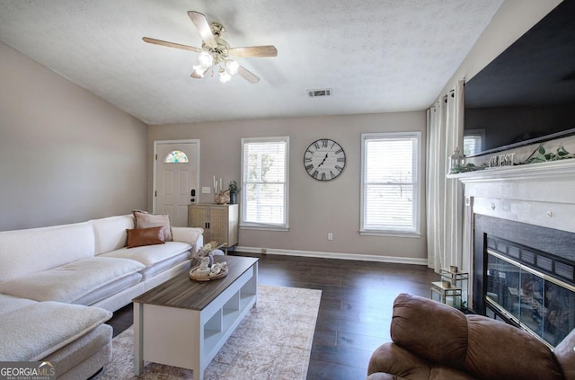 living room featuring visible vents, baseboards, a fireplace, dark wood-style flooring, and a textured ceiling