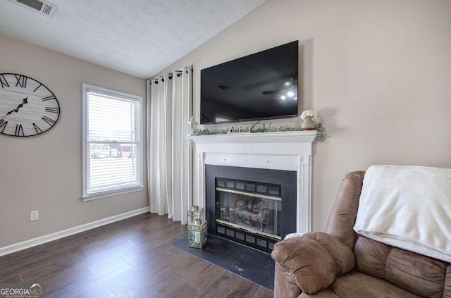 living room featuring wood finished floors, visible vents, baseboards, lofted ceiling, and a fireplace with flush hearth