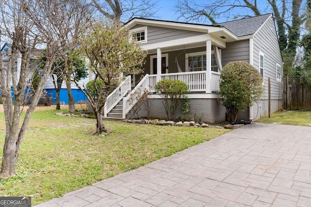 view of front facade with a front yard, covered porch, and roof with shingles