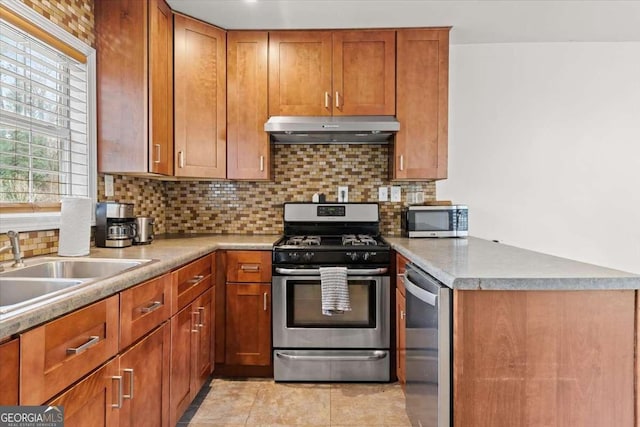 kitchen featuring a peninsula, decorative backsplash, appliances with stainless steel finishes, under cabinet range hood, and brown cabinets