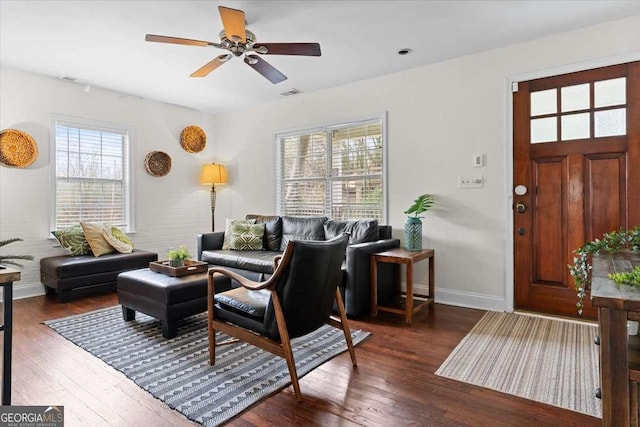 living area featuring dark wood finished floors, baseboards, visible vents, and ceiling fan