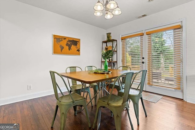 dining room featuring hardwood / wood-style floors, an inviting chandelier, baseboards, and visible vents