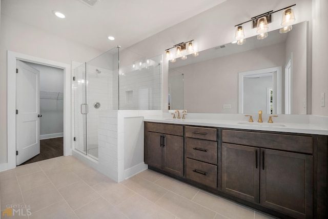 full bath with double vanity, a sink, a shower stall, a walk in closet, and tile patterned floors