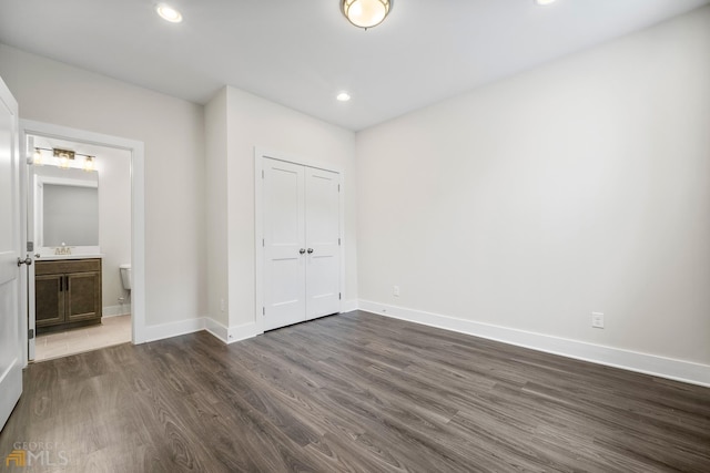 unfurnished bedroom featuring baseboards, ensuite bath, recessed lighting, dark wood-style flooring, and a closet