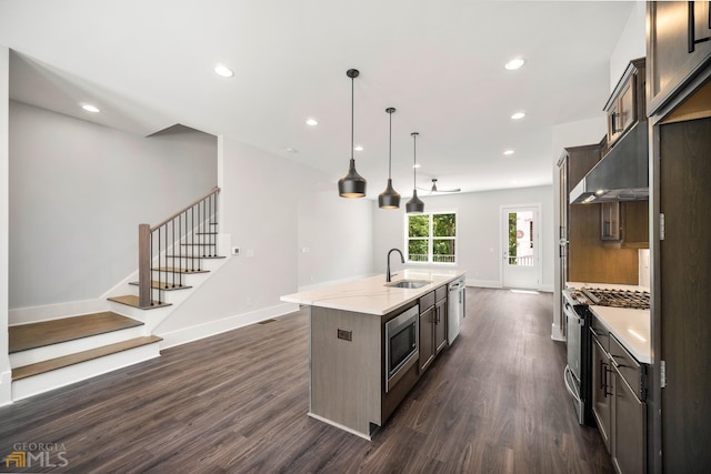 kitchen featuring a center island with sink, dark wood-style flooring, a sink, under cabinet range hood, and appliances with stainless steel finishes