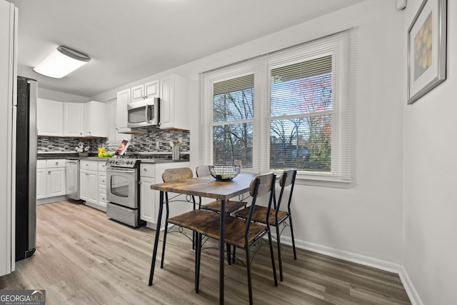 kitchen with light wood-style flooring, backsplash, dark countertops, appliances with stainless steel finishes, and baseboards