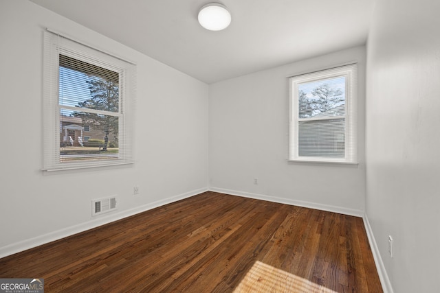 empty room featuring plenty of natural light, baseboards, visible vents, and dark wood-style flooring