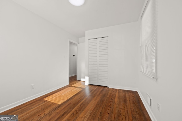 unfurnished bedroom with a closet, baseboards, visible vents, and wood finished floors