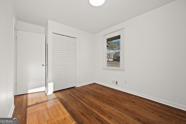 unfurnished bedroom with a closet, visible vents, dark wood-type flooring, and baseboards
