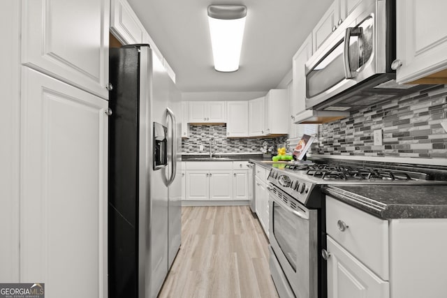 kitchen featuring dark countertops, tasteful backsplash, light wood-style flooring, white cabinets, and stainless steel appliances