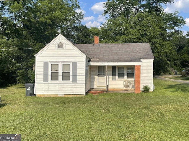 view of front of house with roof with shingles, covered porch, a front yard, crawl space, and a chimney