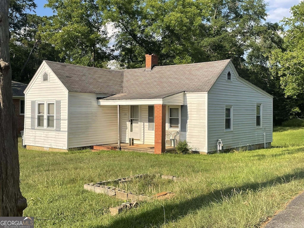 view of front of property with a front yard, a porch, roof with shingles, and a chimney