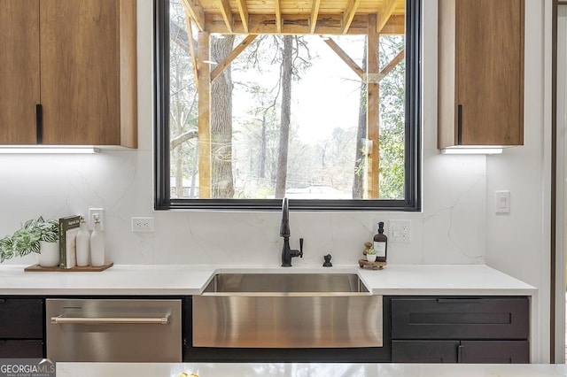 kitchen with backsplash, stainless steel dishwasher, light countertops, and a sink