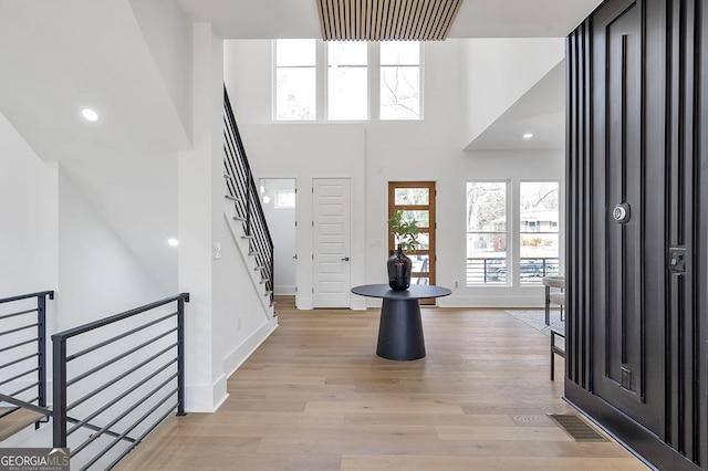 entrance foyer with visible vents, baseboards, a high ceiling, and light wood-style floors