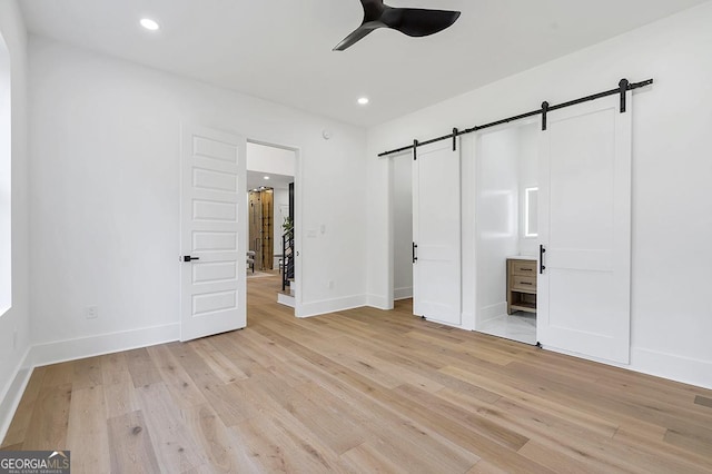 unfurnished bedroom featuring recessed lighting, baseboards, light wood-type flooring, and a barn door