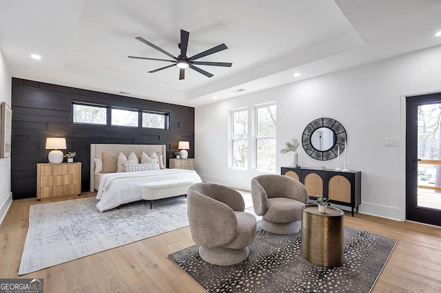 bedroom with multiple windows, light wood-style floors, a tray ceiling, and an accent wall