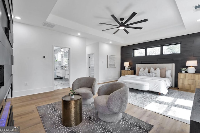 bedroom with a tray ceiling, wood finished floors, and visible vents