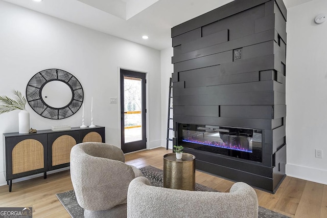 living room with light wood finished floors, a glass covered fireplace, recessed lighting, and baseboards