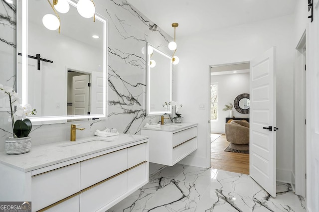 full bath featuring marble finish floor, stone wall, two vanities, and a sink