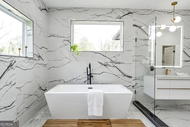 full bath featuring a freestanding tub, marble finish floor, stone wall, and vanity