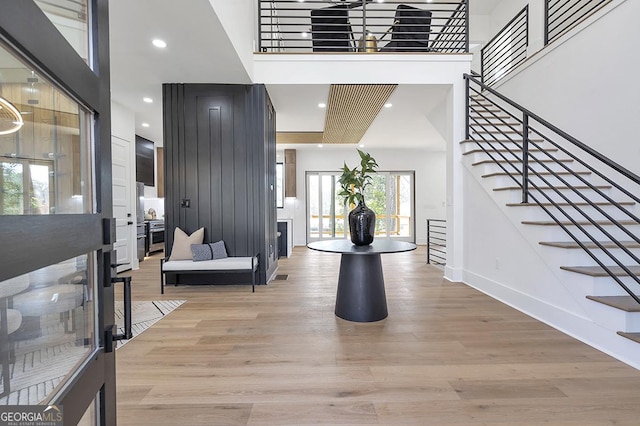 entryway with light wood-style floors, baseboards, stairs, and a towering ceiling