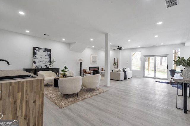 living area featuring a glass covered fireplace, recessed lighting, visible vents, and light wood finished floors