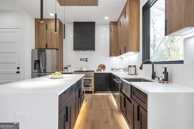 kitchen featuring light wood finished floors, a kitchen island, wall chimney range hood, high end appliances, and light countertops