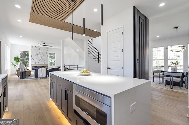 kitchen featuring decorative light fixtures, stainless steel microwave, light wood-type flooring, and ceiling fan