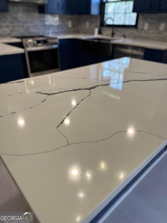 details featuring light stone counters, a sink, decorative backsplash, stainless steel range with electric stovetop, and dark cabinets