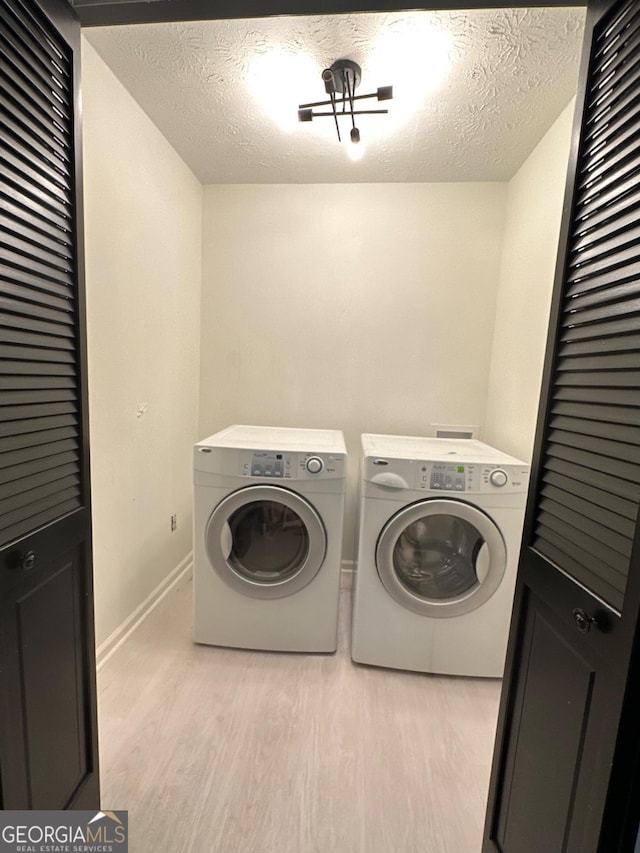 laundry area featuring baseboards, light wood finished floors, washing machine and clothes dryer, laundry area, and a textured ceiling