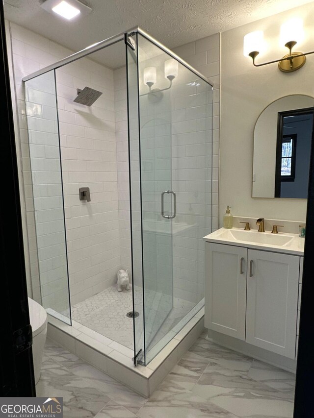 full bathroom featuring vanity, a shower stall, a textured ceiling, toilet, and marble finish floor