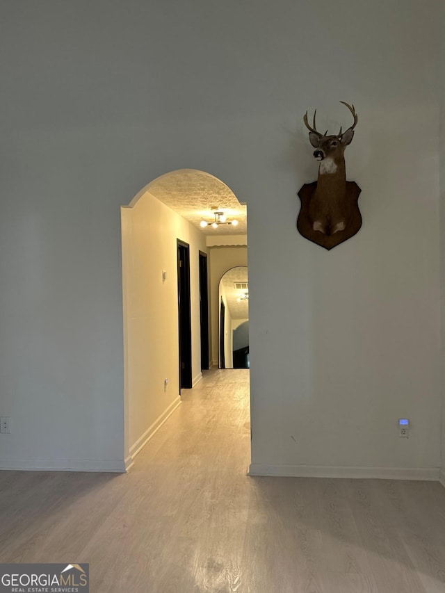 interior space with arched walkways, baseboards, and light wood-style floors