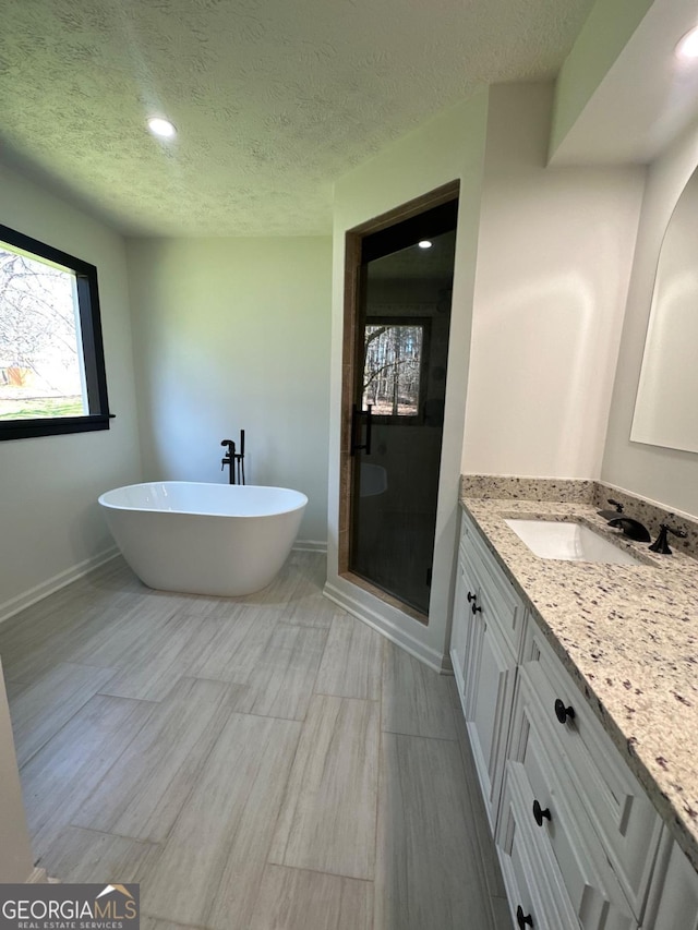 full bath with a textured ceiling, a shower stall, baseboards, a soaking tub, and vanity