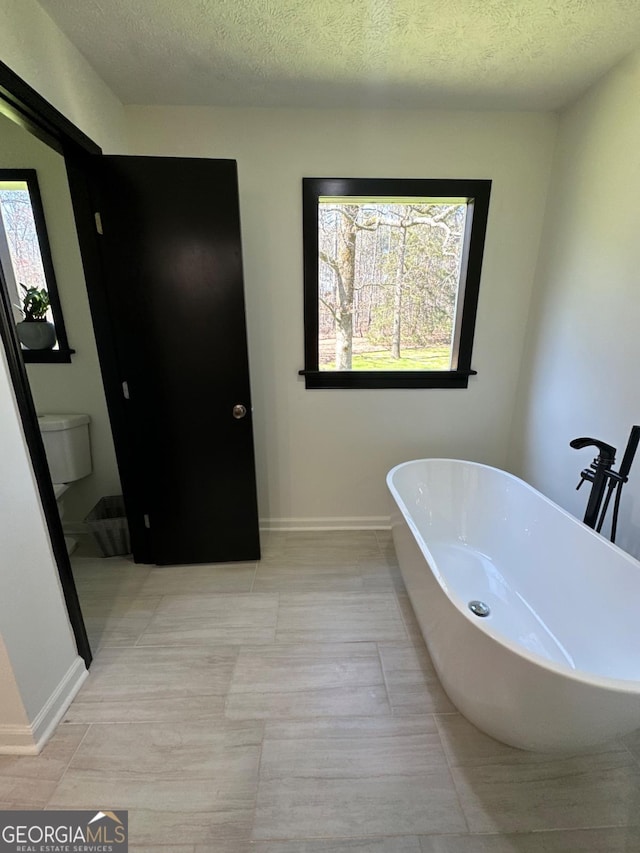 full bath with a soaking tub, toilet, baseboards, and a textured ceiling