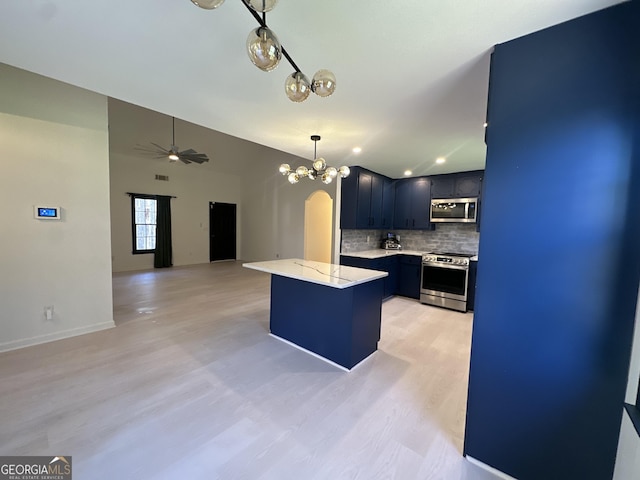 kitchen with decorative backsplash, vaulted ceiling, appliances with stainless steel finishes, ceiling fan with notable chandelier, and light wood-type flooring