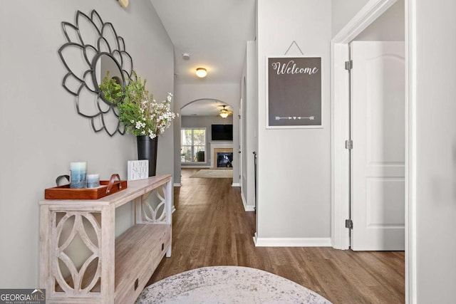 corridor with baseboards, arched walkways, and wood finished floors