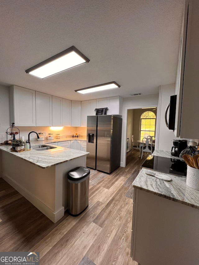 kitchen featuring a sink, white cabinetry, a peninsula, stainless steel fridge with ice dispenser, and light stone countertops