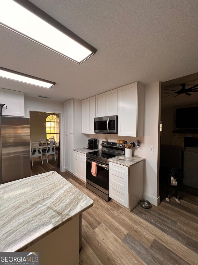 kitchen featuring light stone countertops, appliances with stainless steel finishes, wood finished floors, a textured ceiling, and white cabinetry