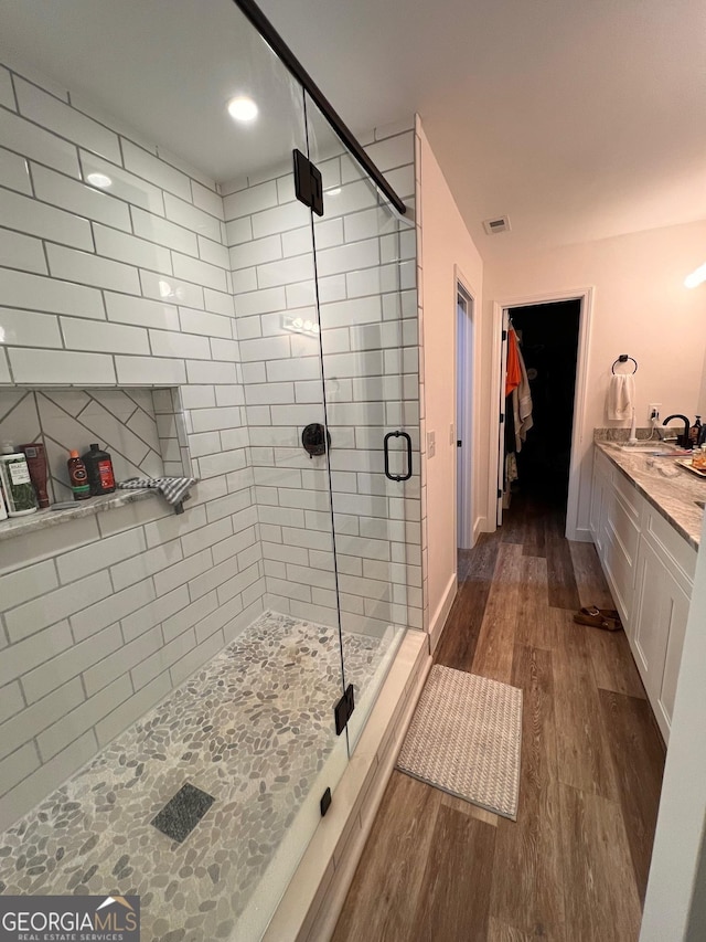 bathroom with vanity, wood finished floors, baseboards, a stall shower, and a spacious closet