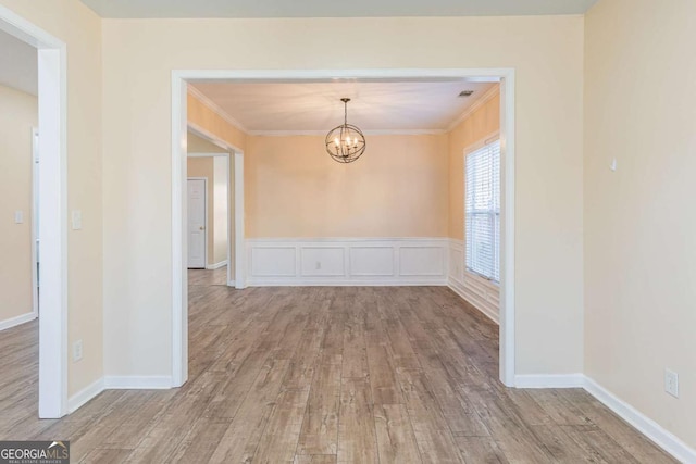 unfurnished dining area featuring an inviting chandelier, crown molding, and wood finished floors