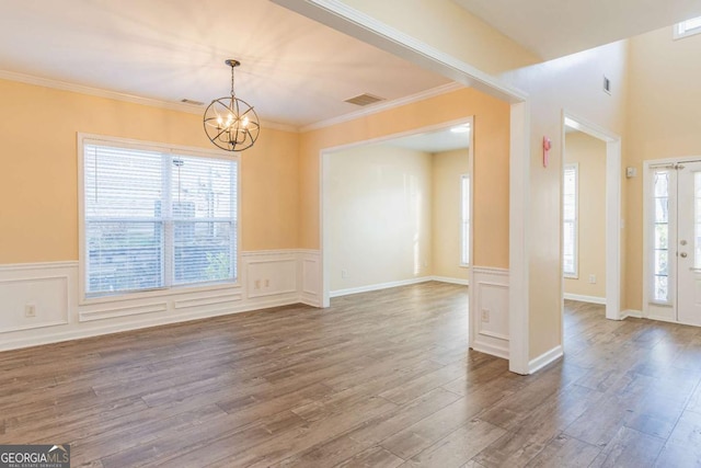 empty room featuring a notable chandelier, a decorative wall, visible vents, and wood finished floors