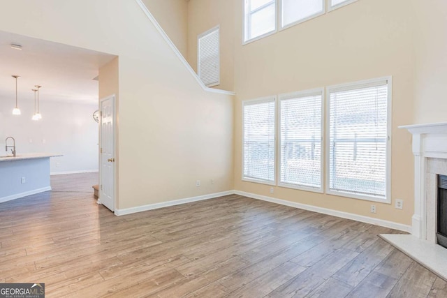 unfurnished living room featuring a sink, baseboards, light wood-style floors, and a fireplace with raised hearth