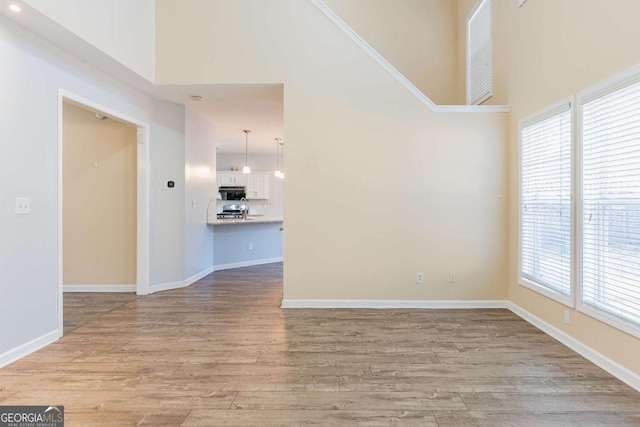 unfurnished room featuring baseboards, light wood-style flooring, and a towering ceiling