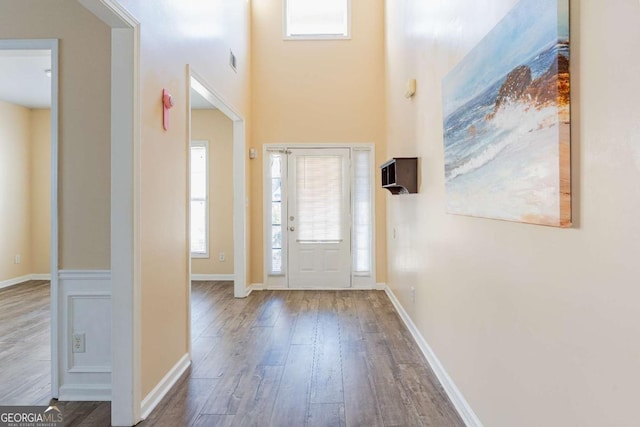 foyer entrance featuring visible vents, baseboards, a high ceiling, and wood finished floors