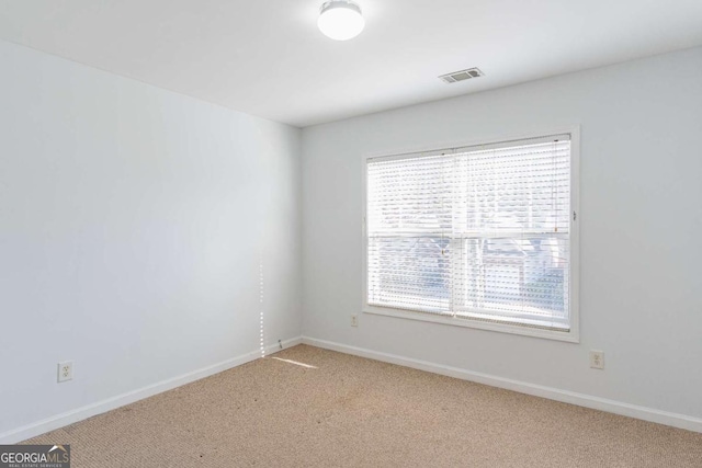 empty room featuring visible vents, light colored carpet, and baseboards