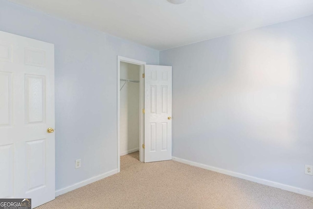 unfurnished bedroom with a closet, light colored carpet, and baseboards