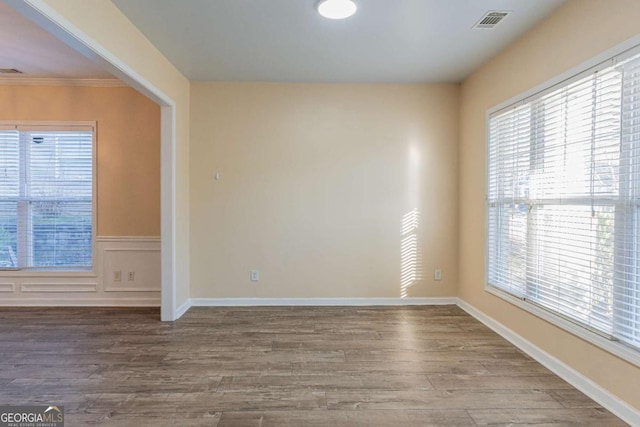 spare room with a decorative wall, wood finished floors, visible vents, and wainscoting