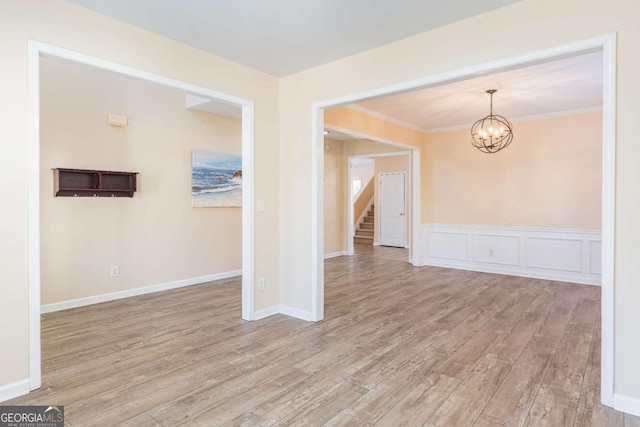 empty room featuring stairway, wood finished floors, crown molding, a decorative wall, and a notable chandelier